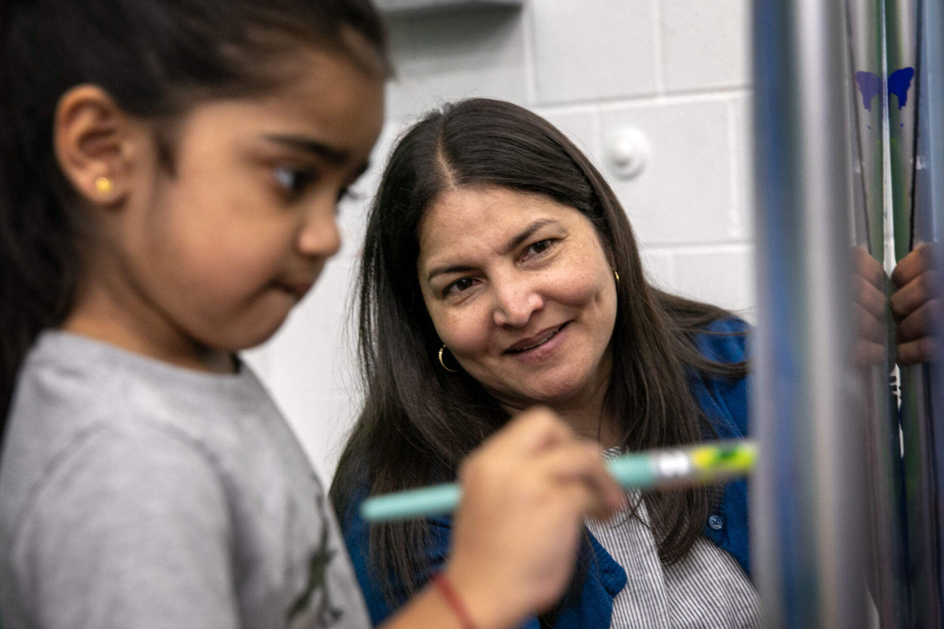 Community Hub Coordinator Lilliana Arteaga watches as a child paints letters on a board at the Mario Umana Academy in East Boston. (Robin Lubbock/WBUR)