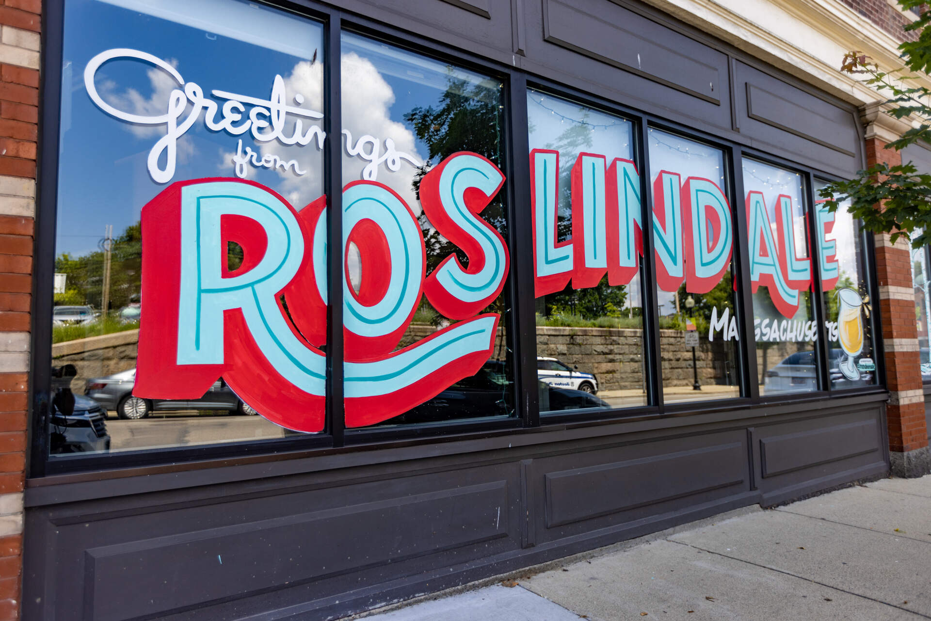 &quot;Greetings from Roslindale, Massachusetts&quot; is painted on the storefront of Distraction Brewing in Roslindale. (Jesse Costa/WBUR)