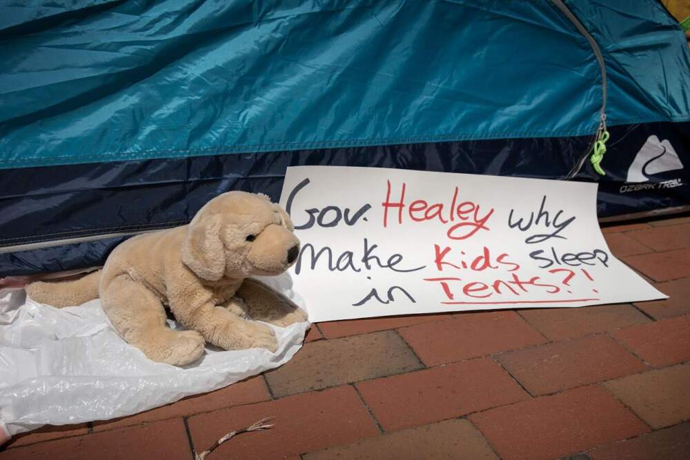 A sign by a tent in front of the Massachusetts State House protests against new restrictions to the family shelter system. (Robin Lubbock/WBUR)