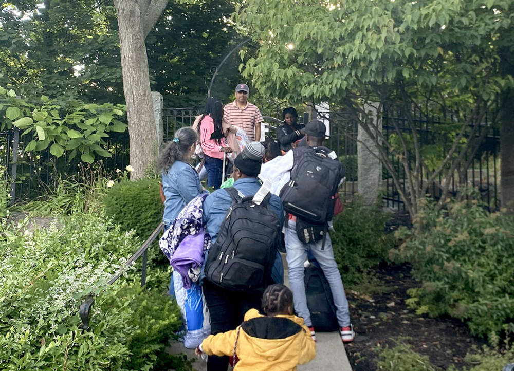 A group of migrants enters the garden of a church in Quincy where they will stay in tents. (Simón Rios/WBUR)