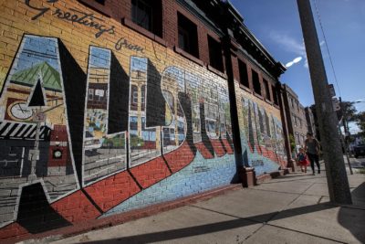 A mother and her daughter walk past the “Greetings from Allston Village” mural on Farrington Street. (Jesse Costa/WBUR)