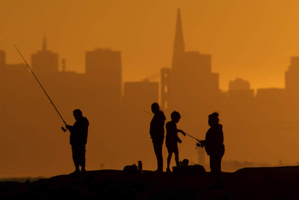 With the San Francisco skyline behind them, people fish off a jetty Monday, July 1, 2024, in Alameda, Calif. An extended heat wave predicted to blanket Northern California has resulted in red flag fire warnings. (/Noah Berger/AP)