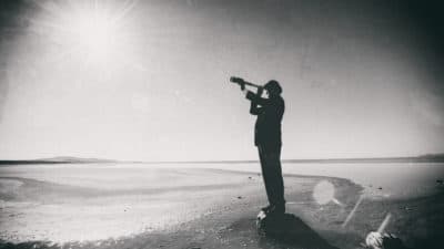 Connoisseur wearing bowler hat looks through spyglass in the dessert. (Ferrantraite/Getty Images)