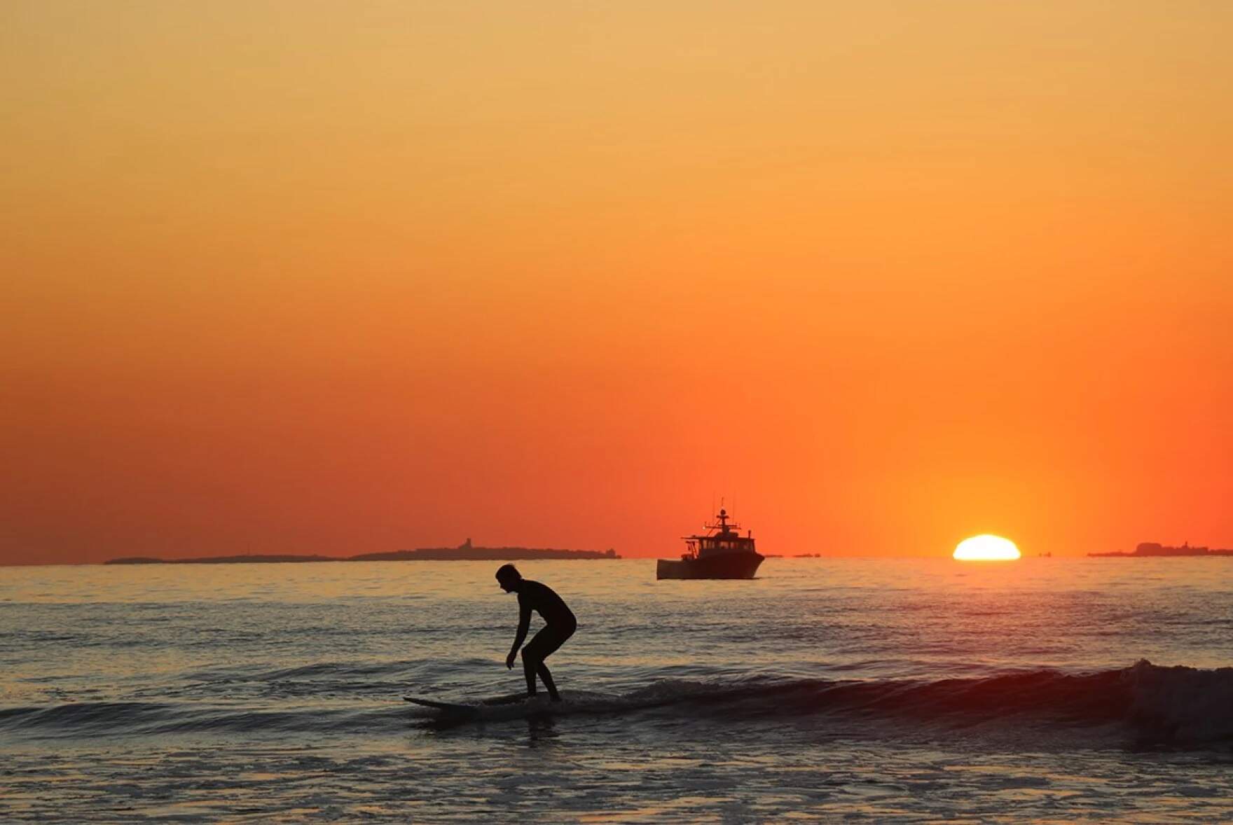 A surfer and fishing vessel make the most of a September morning at sunrise in Rye. (Dan Tuohy/NHPR)