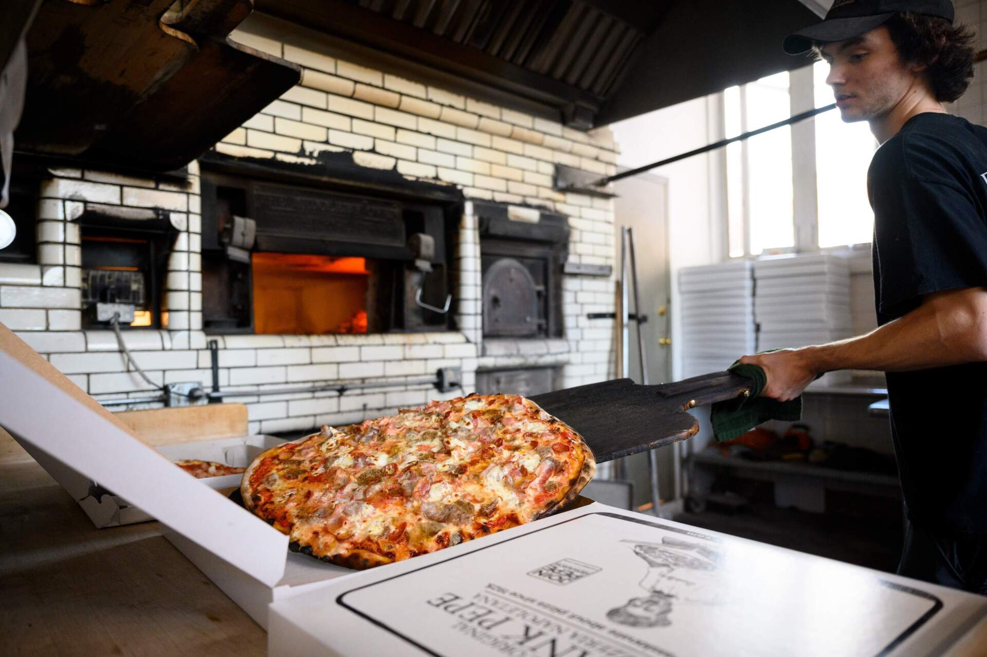 A worker at Frank Pepe Pizzeria Napoletana puts a hot pizza into a to-go box. The restaurant was founded in 1925 by Italian immigrant Frank Pepe in New Haven, and has since opened locations across the Northeast. (Ryan Caron King/Connecticut Public)